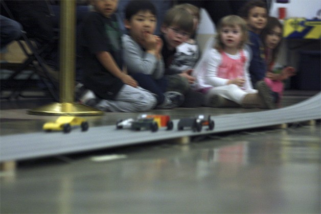 Youngsters look on as Pinewood Derby cars run in a heat.