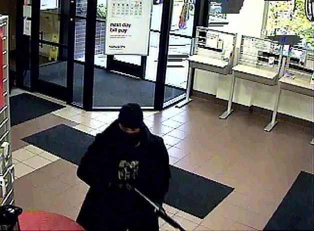 A man wears a dark ski mask and dark clothing during the robbery.